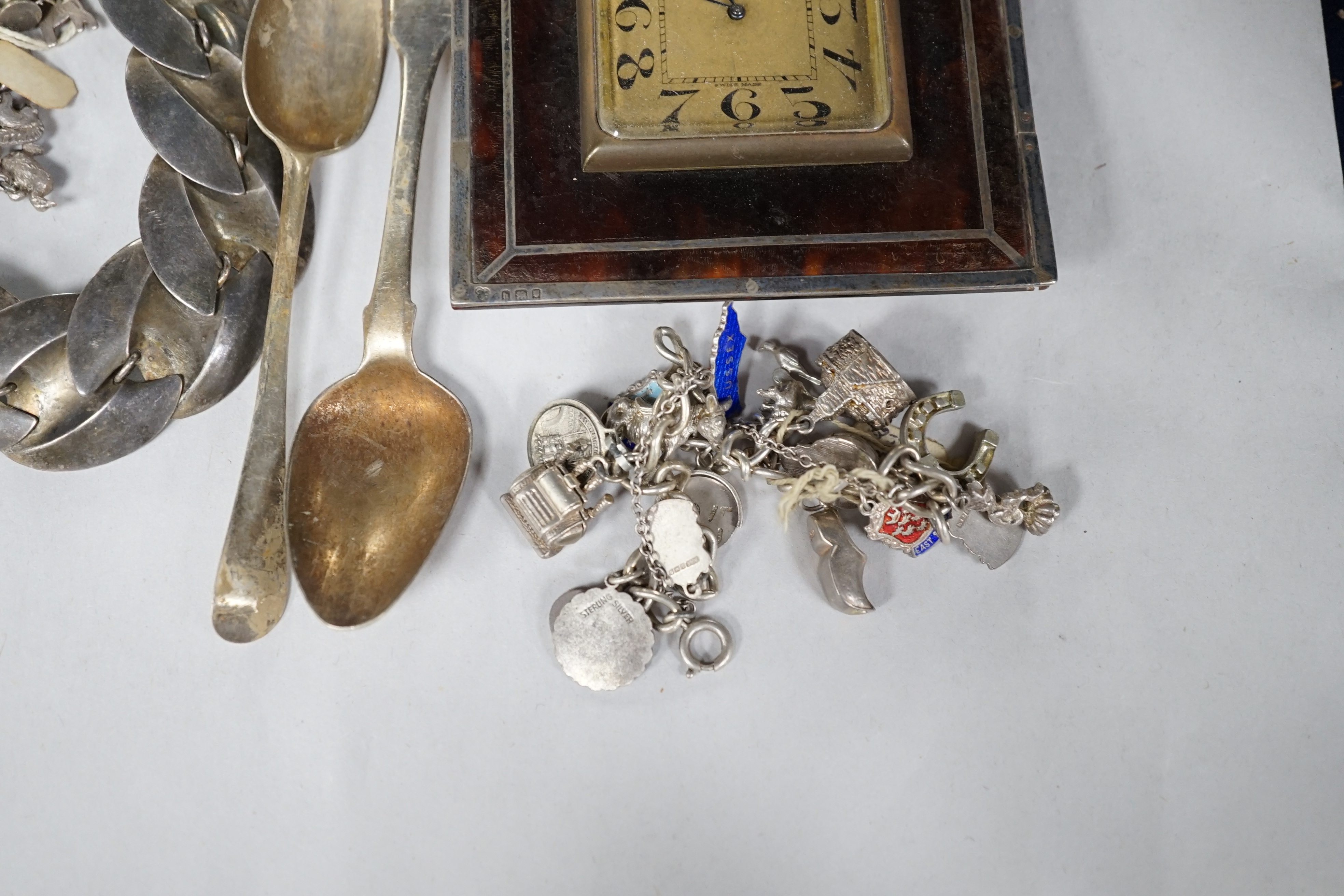 A silver charm bracelet, hung with assorted charms, some hallmarked, one other white metal charm bracelet, a stylish white metal necklace, two silver teaspoons and a George V silver and tortoiseshell mounted timepiece, L